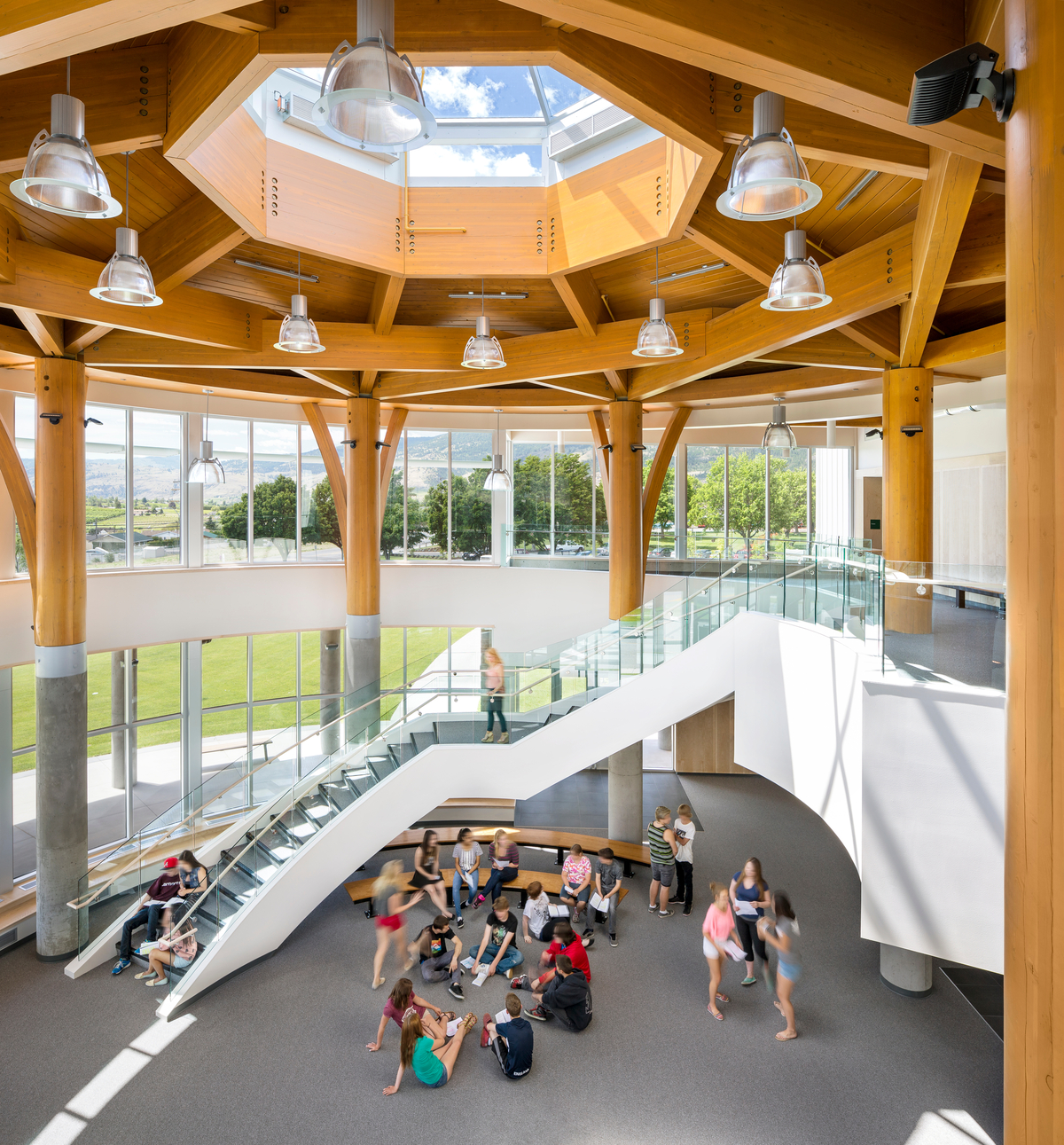 The mass timber ceiling of the Southern Okanagan Secondary School 3 storey atrium, including massive octagonal skylight, natural hewn pillars, and glue-laminated timbers are featured in this image