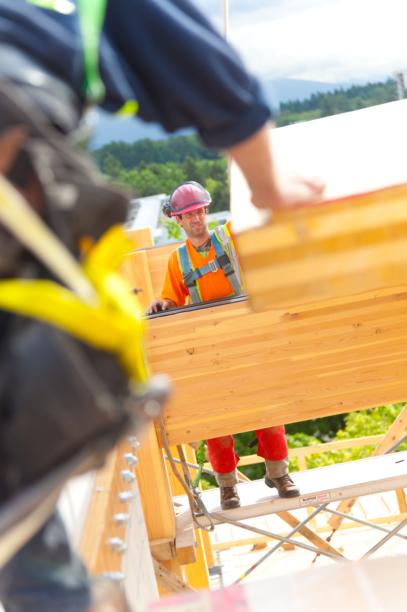Mass timber construction site with worker on scaffolding standing adjacent to Glue-laminated timber (Glulam) beam