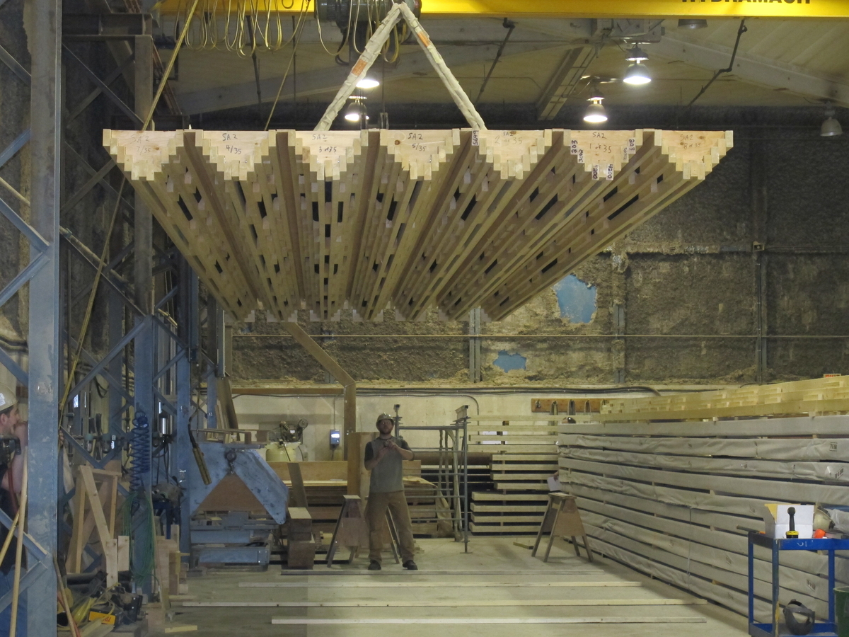 Prefabricated lumber panels are shown suspended by a bridge crane as part of the construction process at the mass timber factoryPrefabricated lumber panels are shown suspended by a bridge crane as part of the construction process at the mass timber factory