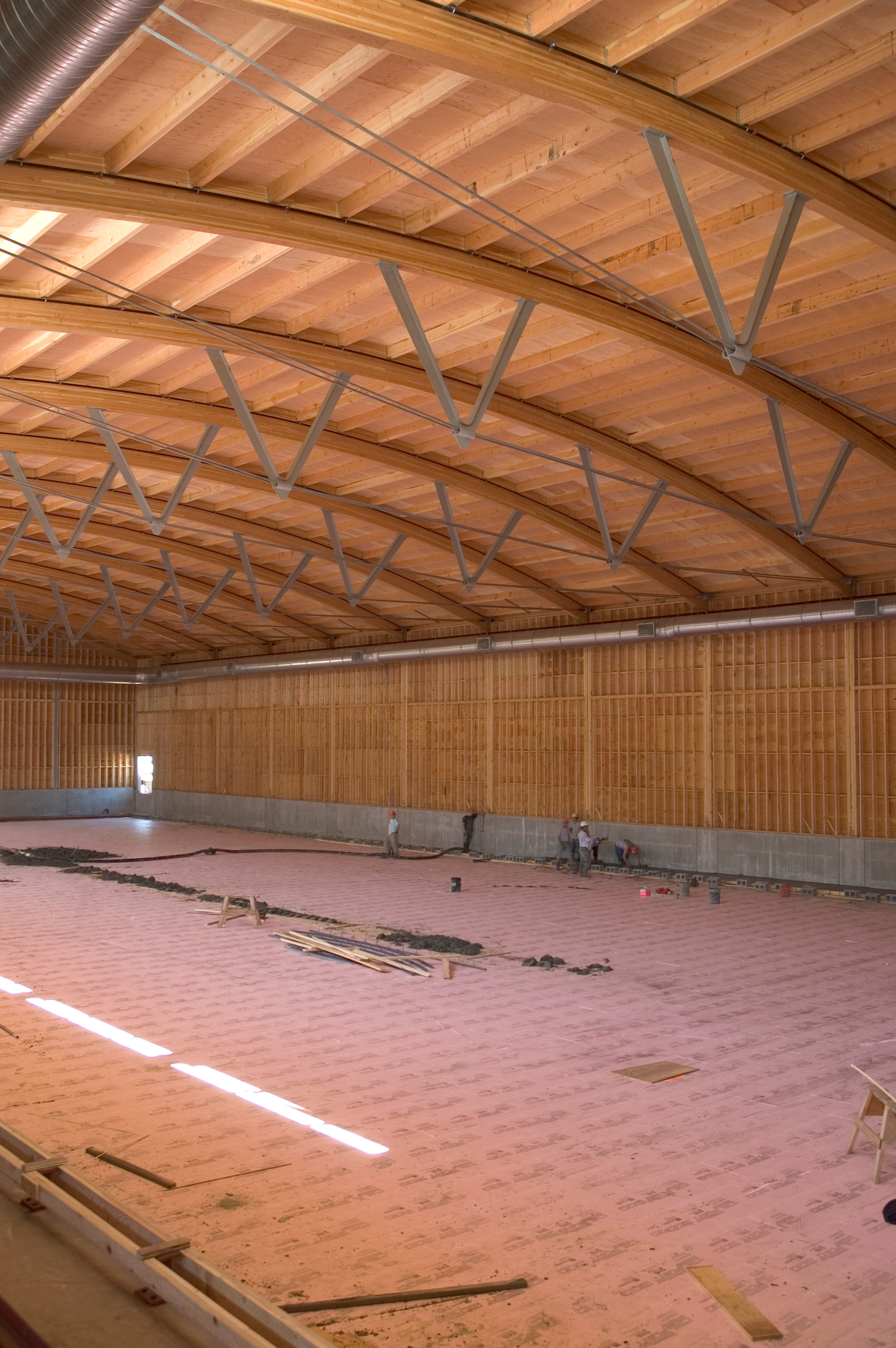 Interior daytime view of Armstrong-Spallumcheen Arena showing arched glue-laminated (Glulam) beams with wood truss and plywood roof above and prefabricated wooden panel walls below