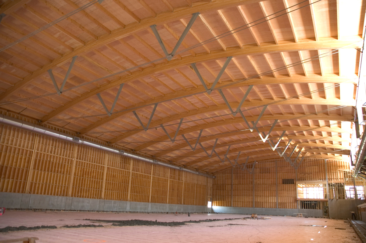 Interior daytime view of Armstrong-Spallumcheen Arena showing arched glue-laminated (Glulam) beams with wood truss and plywood roof above and prefabricated wooden panel walls below