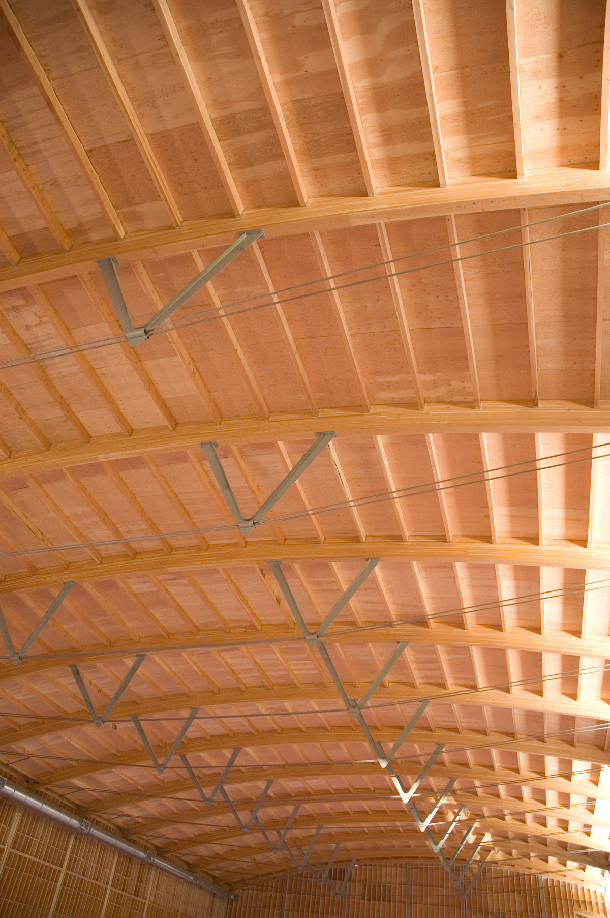 Close up daytime view inside Armstrong-Spallumcheen Arena showing arched glue-laminated (Glulam) beams, tension cables, and steel cable guides