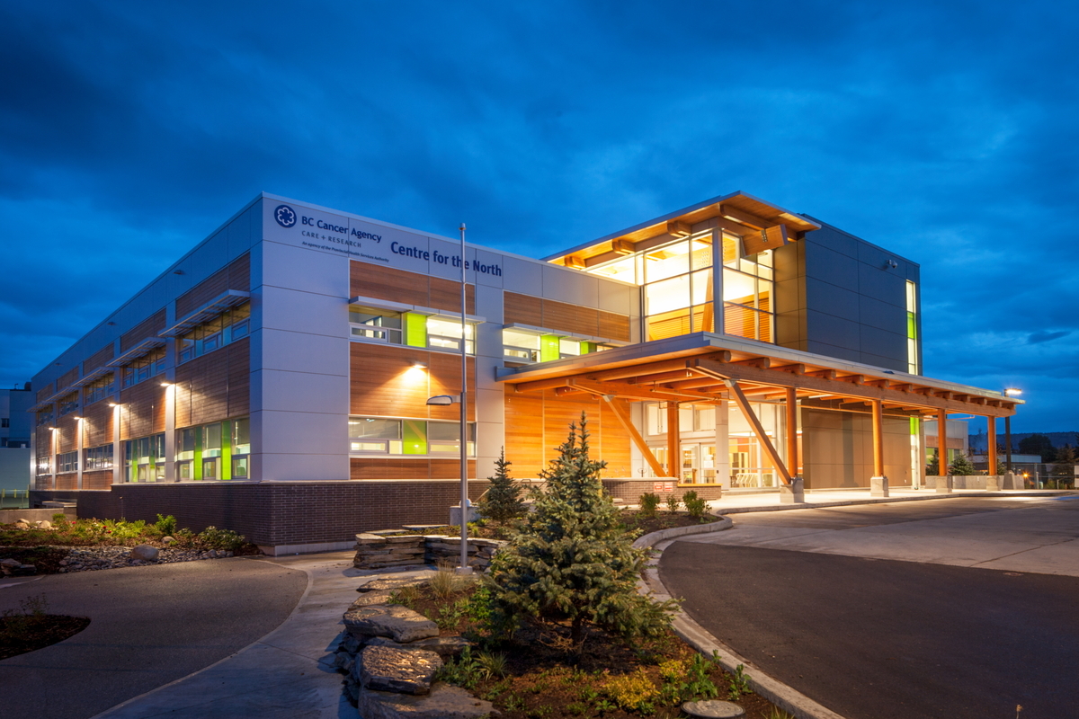 Exterior evening view of low rise BC Cancer Agency Centre for the North showing glue-laminated (glulam) timber, solid-sawn heavy timber, wood paneling and siding