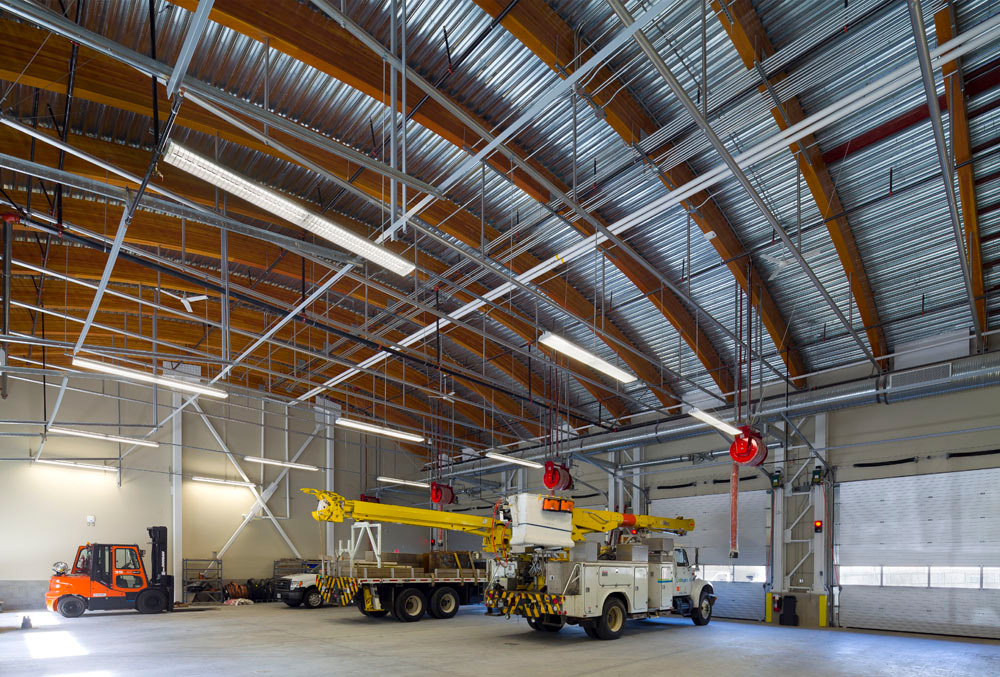 Daytime interior view of BC Hydro Maintenance and Operations Facility in Maple Ridge, BC showing vehicle maintenance bays with curved glue-laminated timber (glulam) timber roof beams topped with a metal clad exterior roof surface visible above
