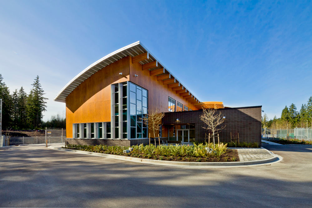 Sunny daytime exterior view of 2,100 square metre two storey BC Hydro Operations Centre in Port Alberni showing wood exterior, including office area with a roof of braced, steel frame supporting glue-laminated timber (glulam) beams on the main column lines
