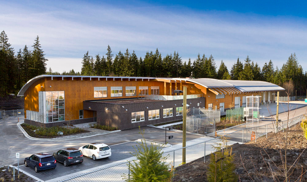 Sunny daytime exterior view of BC Hydro Maintenance and Operations Facility in Maple Ridge, BC showing hybrid & passive house construction using glue-laminated timber (glulam) timber, Solid-sawn heavy timber, and curved roof beams topped with a metal clad exterior roof surface