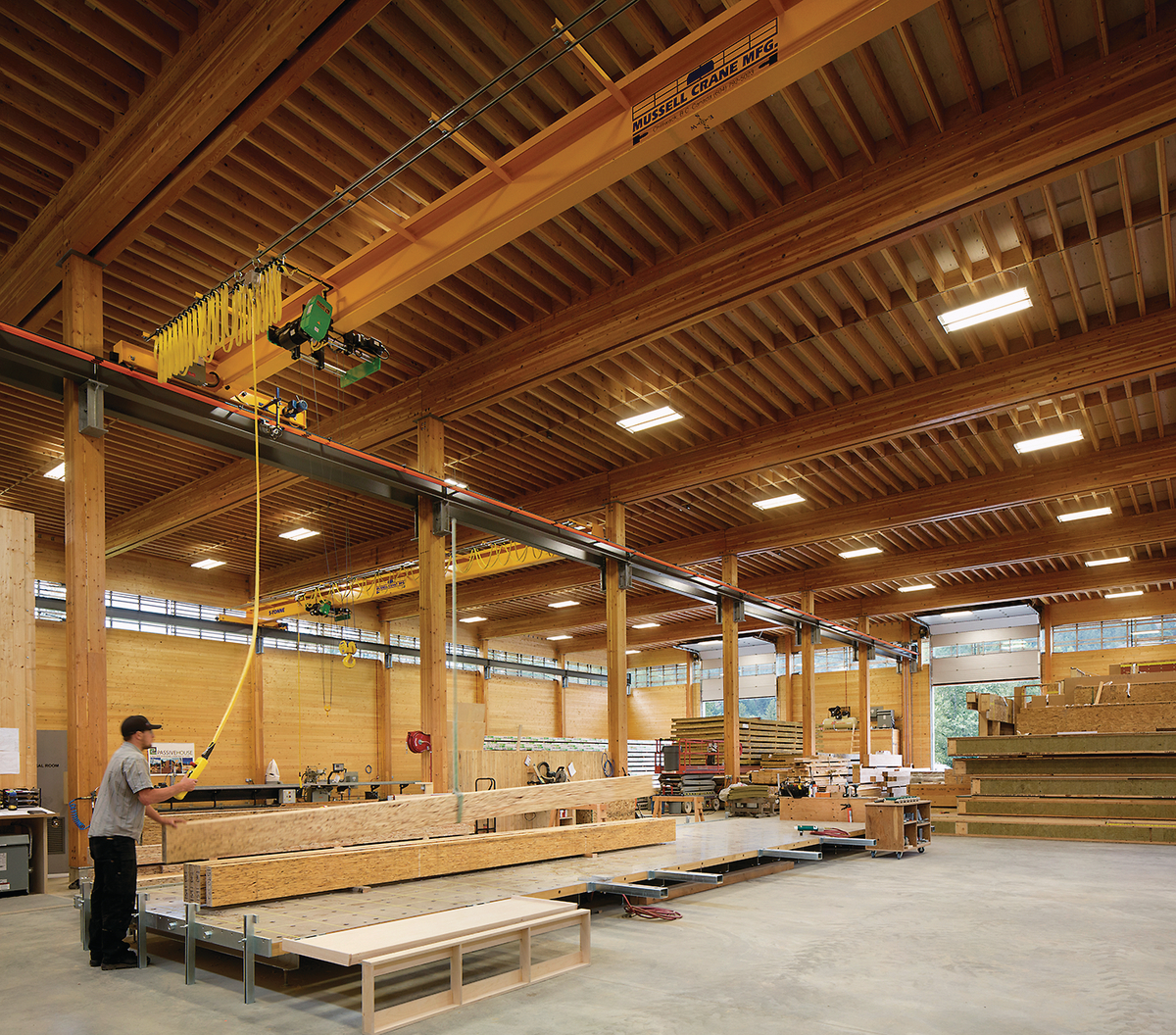Interior view of BC Passive House Factory showing worker using bridge crane to move mass timber beams