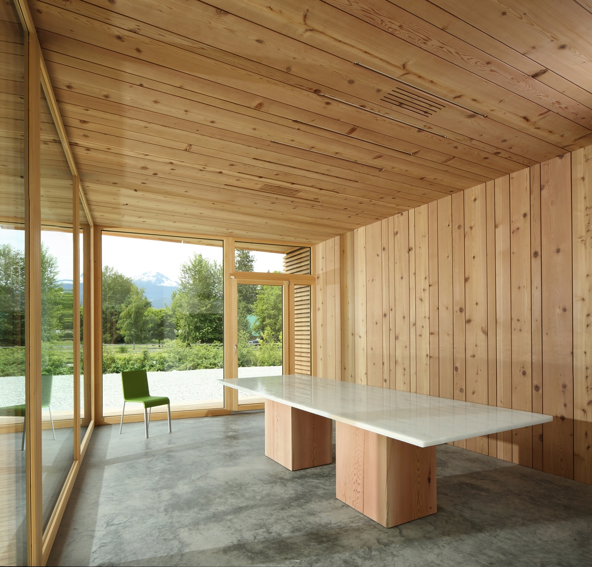 Interior afternoon view of BC Passive House Factory meeting room showing wood wall paneling and wood ceiling paneling with large glass expanses looking outward