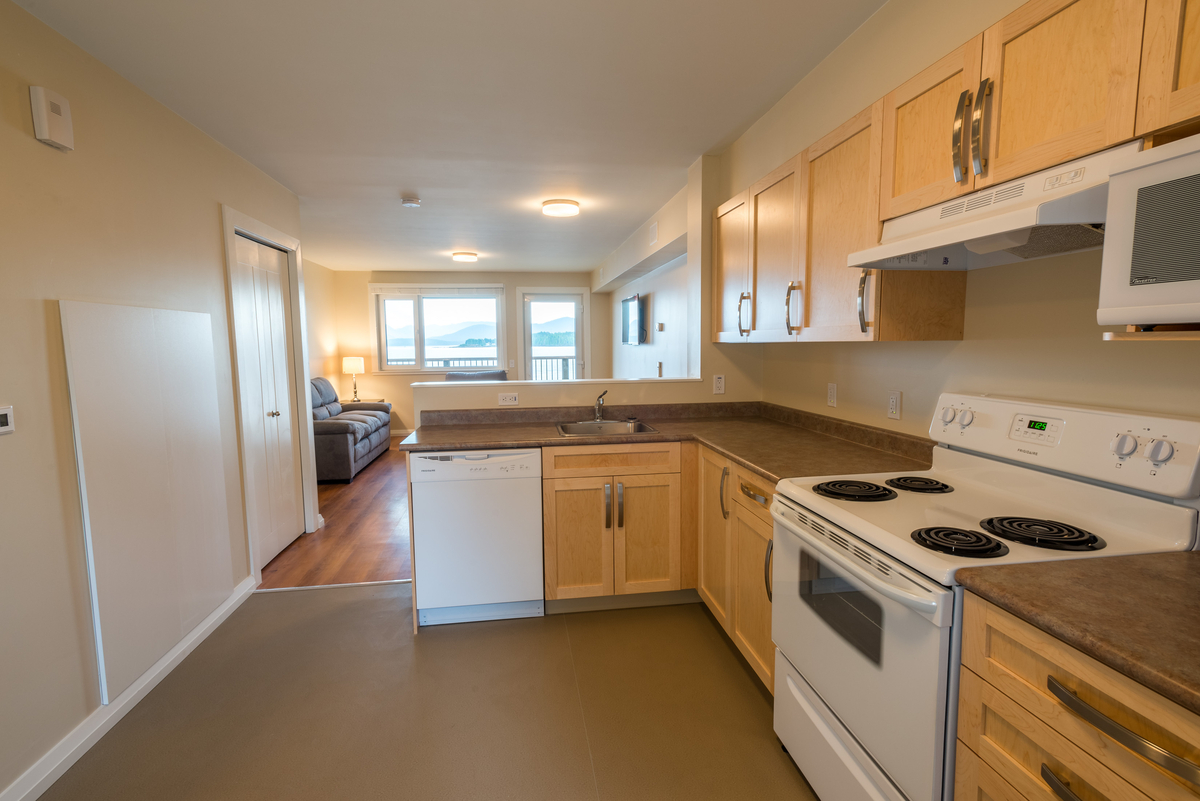 Interior daytime view of modular passive house / high performance Bella Bella Staff Housing, showing white painted wood trim, natural tan kitchen cabinets and contemporary design features