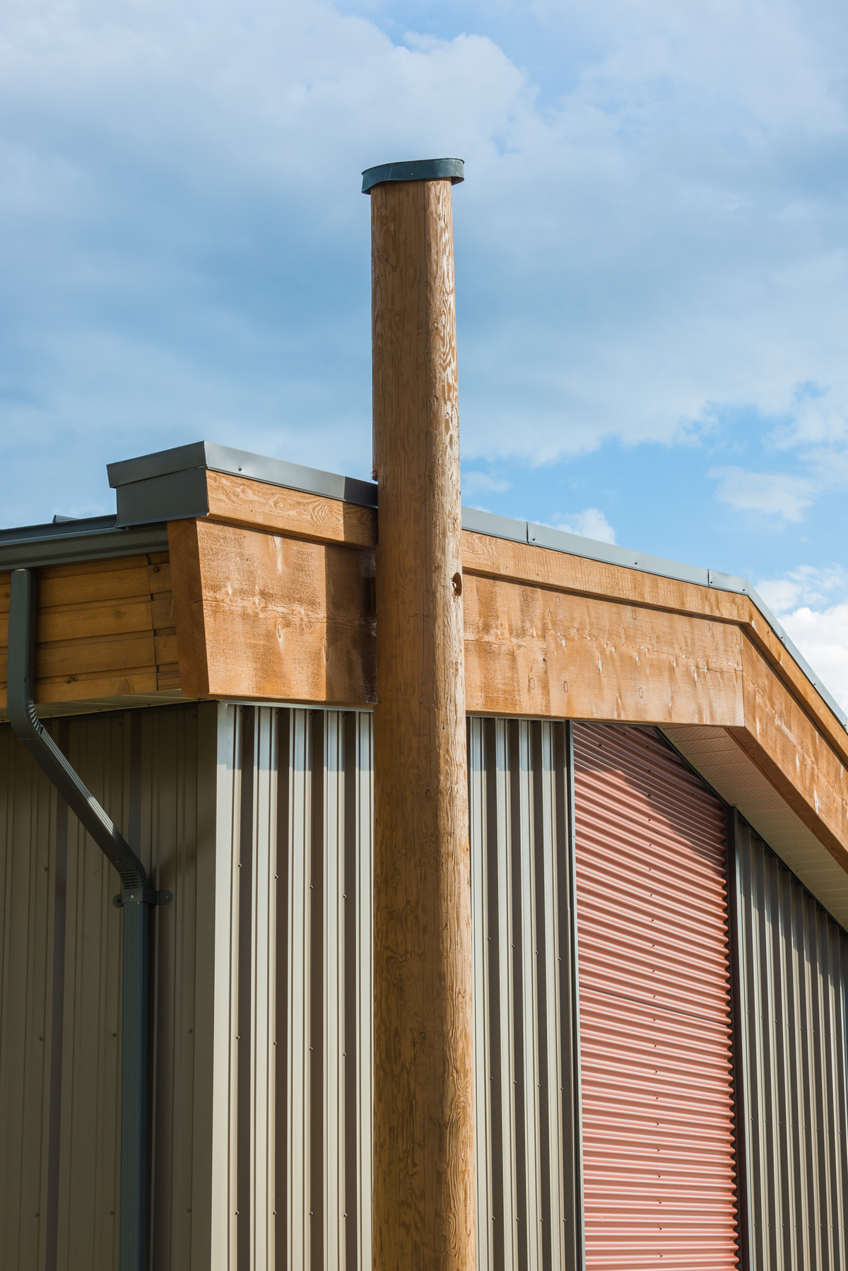 Exterior afternoon view of modular passive house / high performance Bella Bella Staff Housing, showing close up of vertical log pole and side of building with steel and solid-sawn heavy timber