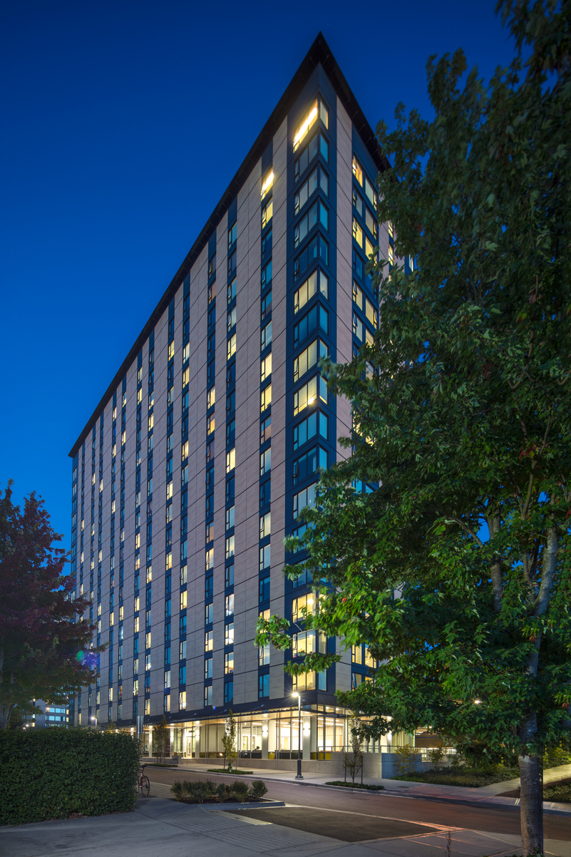 Exterior ground up night time view of completed and occupied Brock Commons Tallwood House showing prefabricated exterior wall panels and warm glowing lights from within