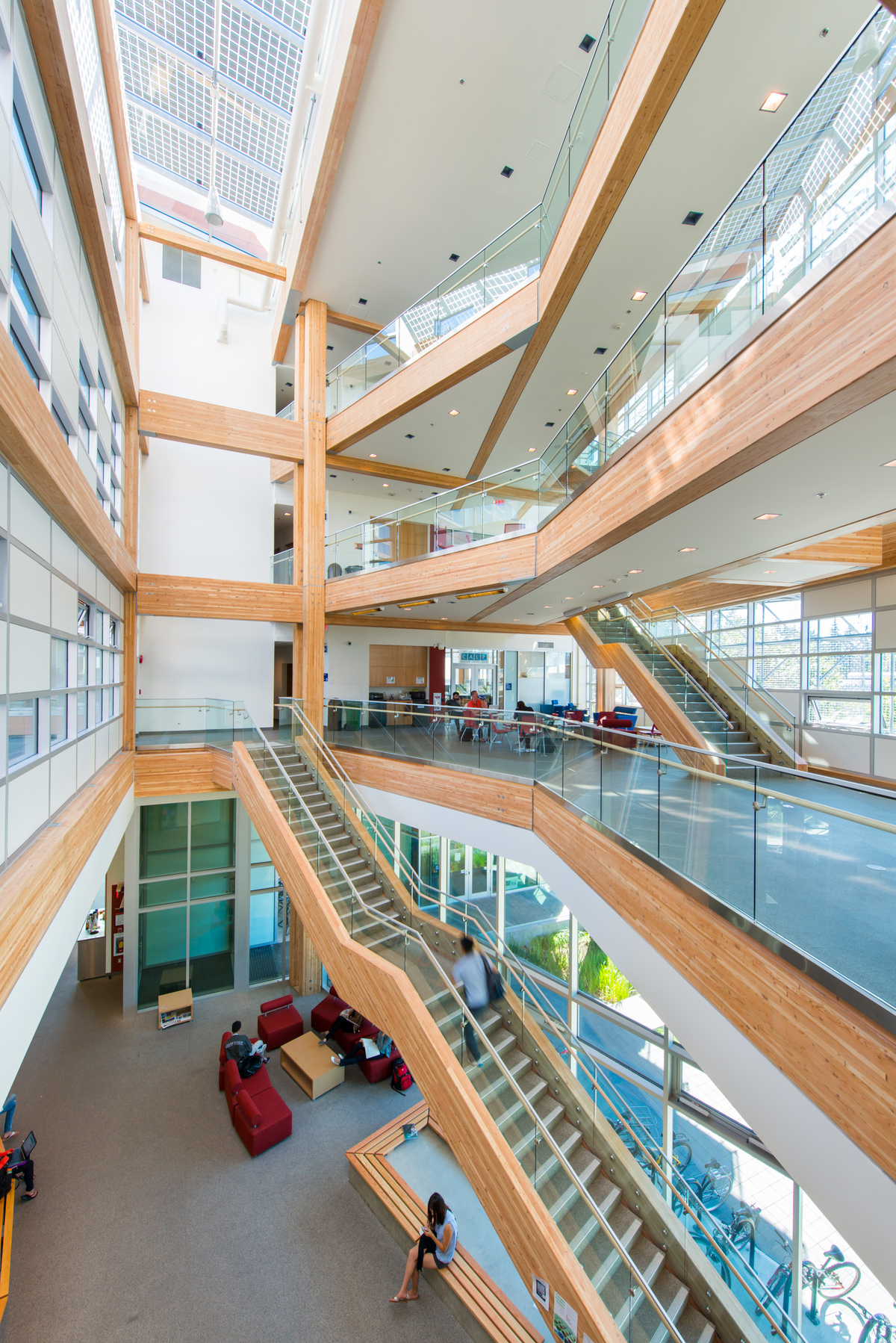 Interior vibrant daytime image of UBC Centre for Interactive Research on Sustainability (CIRS) glass fronted main atrium, showing multi storey stairs, balconies, and columns, all using Glue-laminated timber (Glulam) structural members