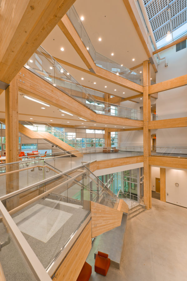 Interior vibrant daytime image of UBC Centre for Interactive Research on Sustainability (CIRS) glass fronted main atrium, showing multi storey stairs, balconies, and columns, all using glue-laminated timber (Glulam) structural members