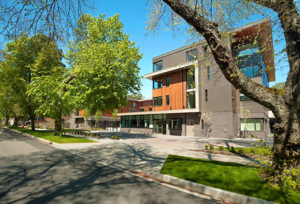 Exterior sunny view of three-storey low rise mass timber constructed Camas Gardens Supported Housing showing warm exterior of Western Red Cedar from across street