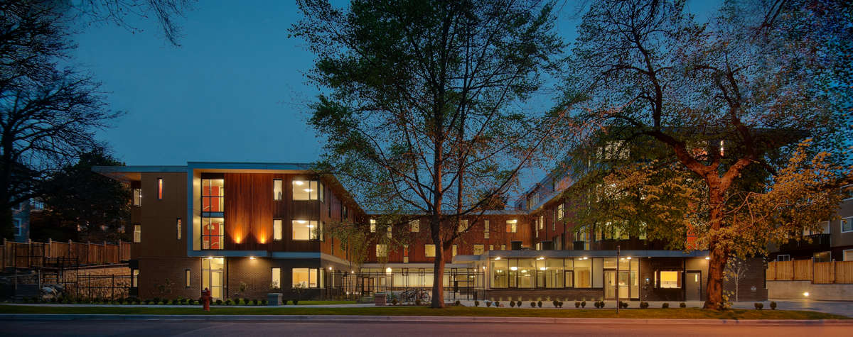 Exterior nighttime view of three-storey low rise mass timber constructed Camas Gardens Supported Housing showing warm exterior of Western Red Cedar from across street