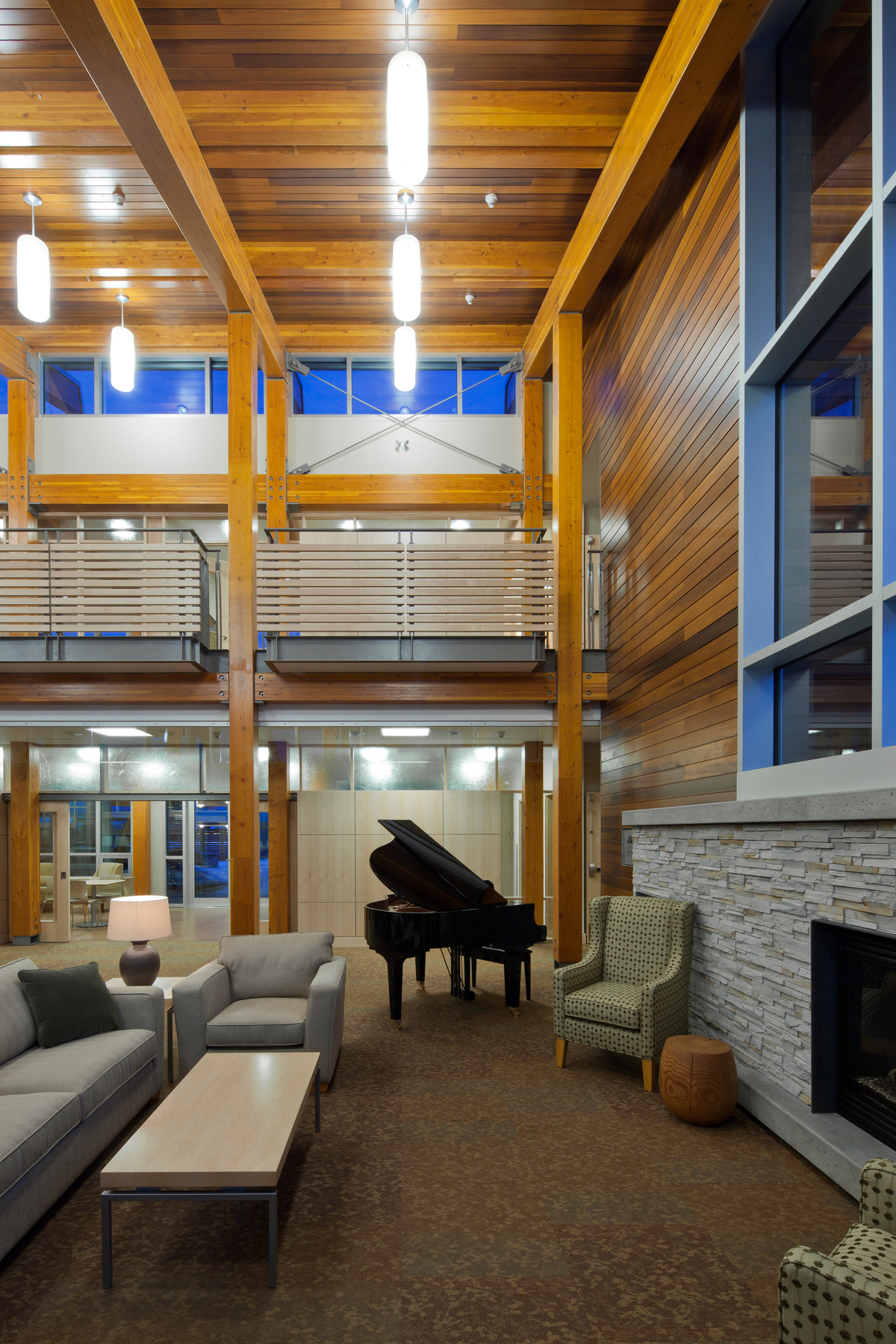 Interior evening social area view inside low rise two story Canadian Cancer Society Kordyban Lodge, showing glue-laminated timber (Glulam), and decorative siding
