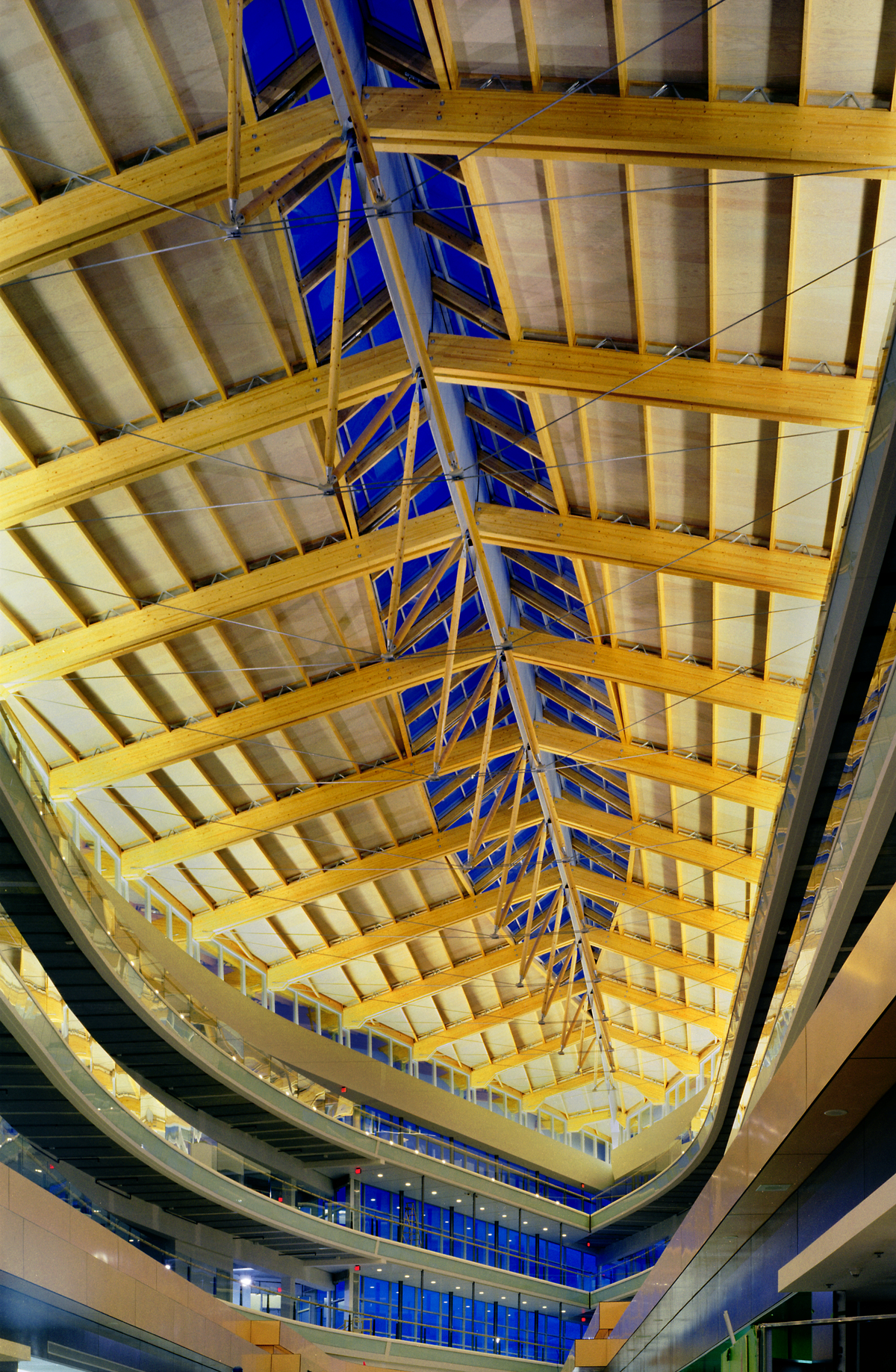 Interior evening view of Surrey Central City ceiling structure showing steel tensioning cables, glue-laminated timber (Glulam) beams, and central glass and wood ridge