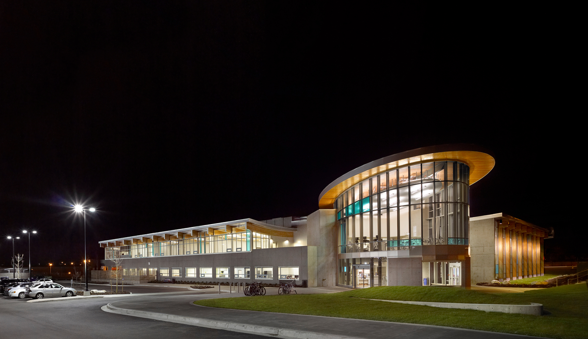 Exterior nighttime image of glass, wood, and concrete hybrid low rise Cloverdale Recreation Centre showing glue-laminated timber (Glulam) and post + beam structural members