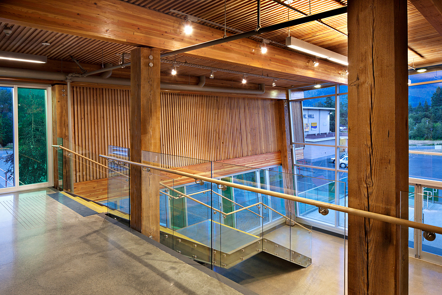 Interior upper floor evening view of low rise Cowichan Lake Sports Arena, showing main entrance constructed with heavy timber, glue-laminated timber (glulam) beams, wood paneling