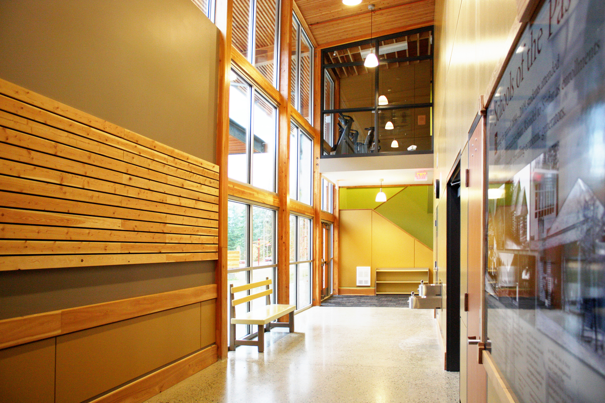 Interior view of low rise Crawford Bay Elementary-Secondary School two storey atrium hallway showing hybrid construction utilizing paneling, post + beam, and a roof of stacked wood planks