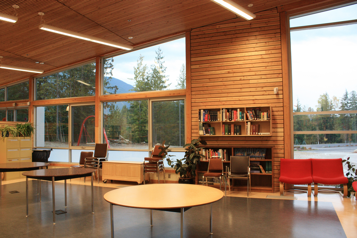 Interior afternoon view of low rise Crawford Bay Elementary-Secondary School library showing abundant use of wood, including window frames, wall paneling, ceiling paneling, and additional millwork