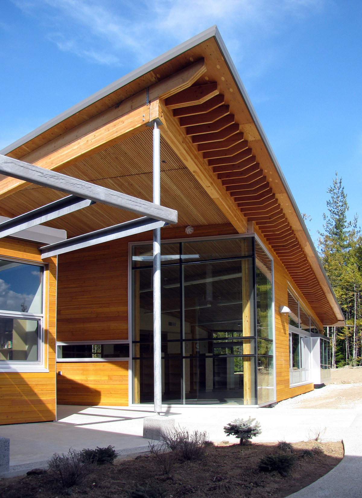 Exterior view of low rise Crawford Bay Elementary-Secondary School showing hybrid construction with significant wood use, including paneling, post + beam, and a roof overhang prefabricated on site from stacked wood planks and glulam beams