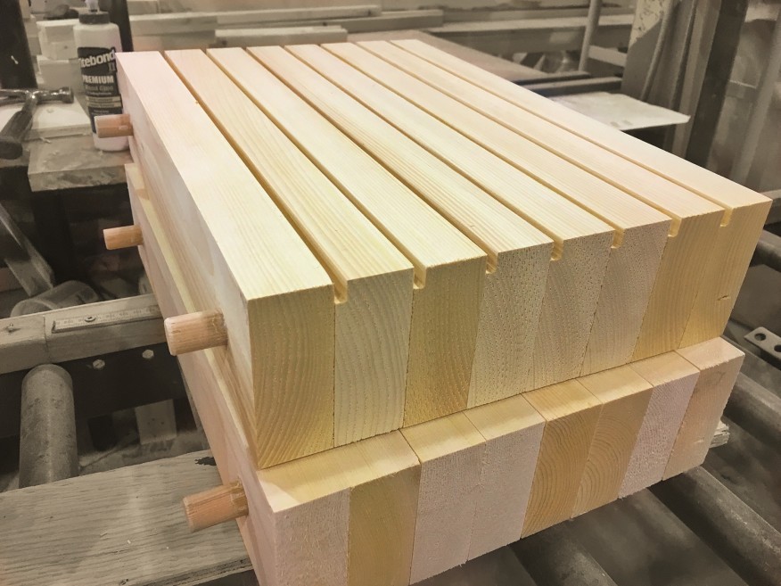 Two sections of dowel-laminated timber (DLT) during construction, showing machinery, glue, and nearly completed DLT sections with dowels protruding