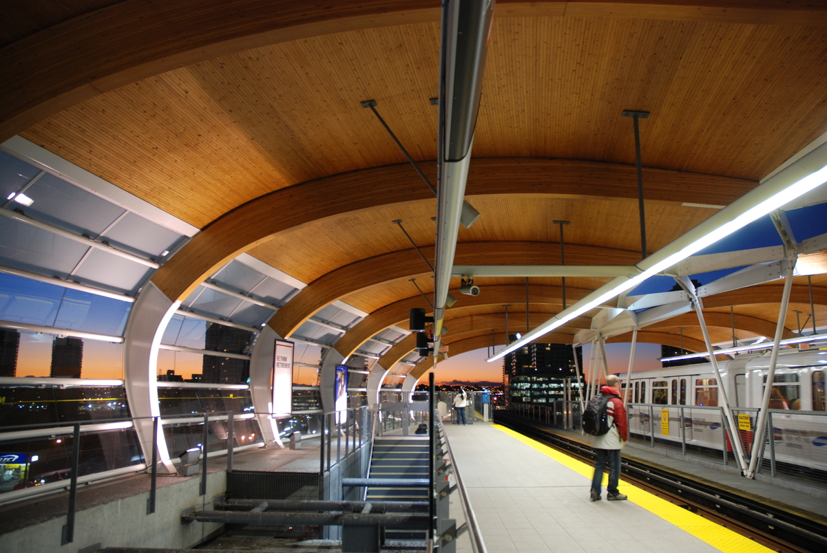 Large arching nail laminated timber (NLT) beams supporting a wooden ceiling are prominent features in this interior view of the City of Burnaby's Brentwood transit station