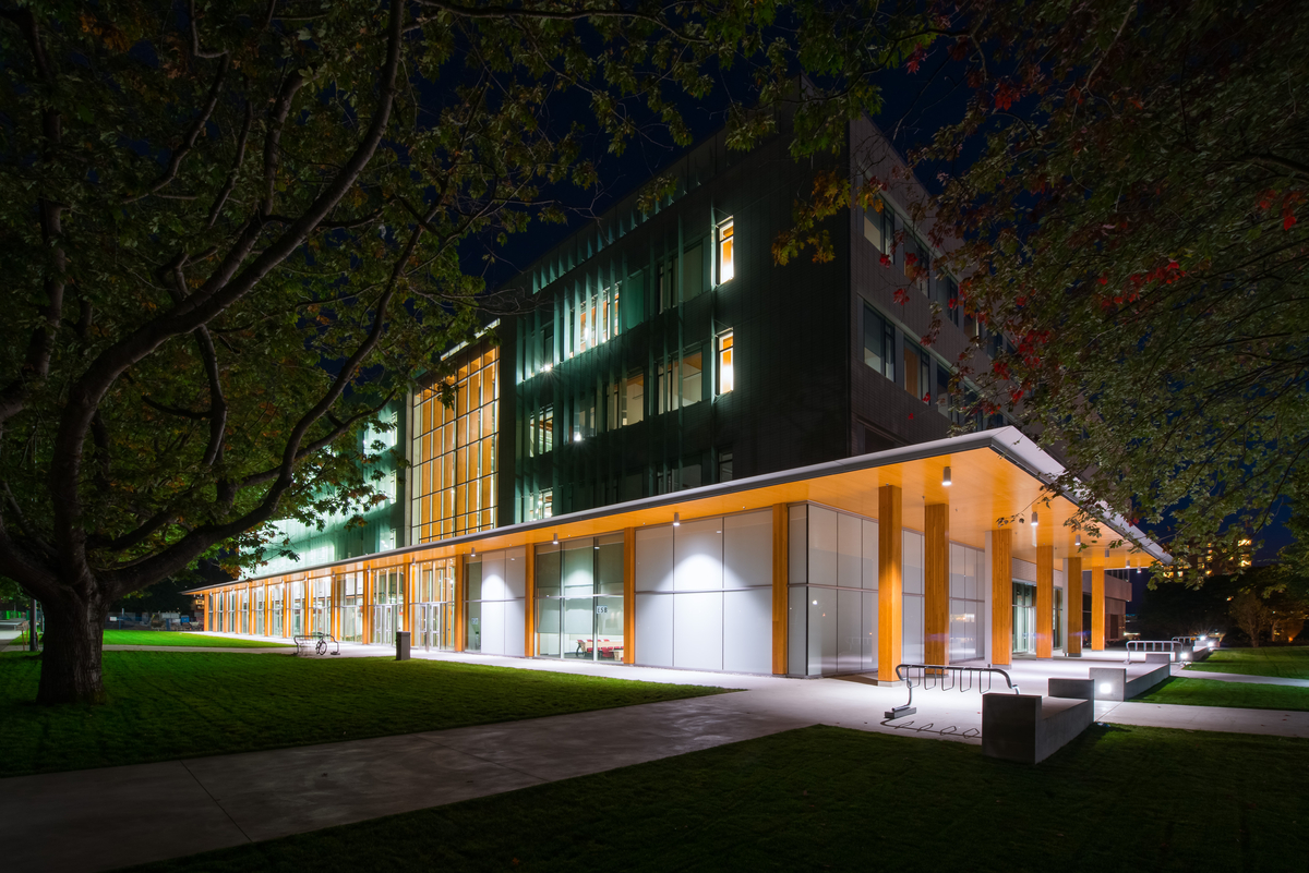 Exterior evening view of mid rise passive house / high performance Earth Sciences Building on UBC Campus showing a perimeter of Glue-laminated timber (Glulam) columns supporting Cross laminated timber (CLT) soffits