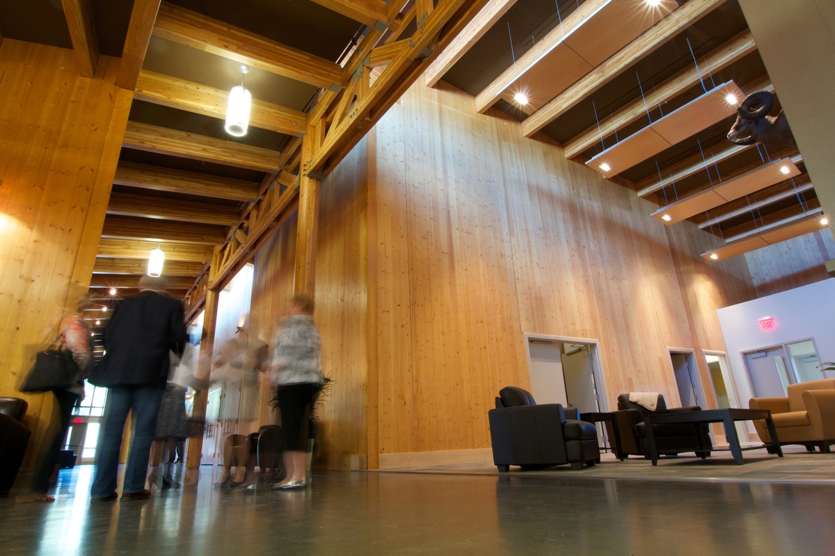 Interior daytime view of Elkford Community Conference Centre showing hallway and people standing below warm structural elements of glue-laminated timber (Glulam) and Laminated veneer lumber (LVL) beams, along with cross-laminated timber (CLT)