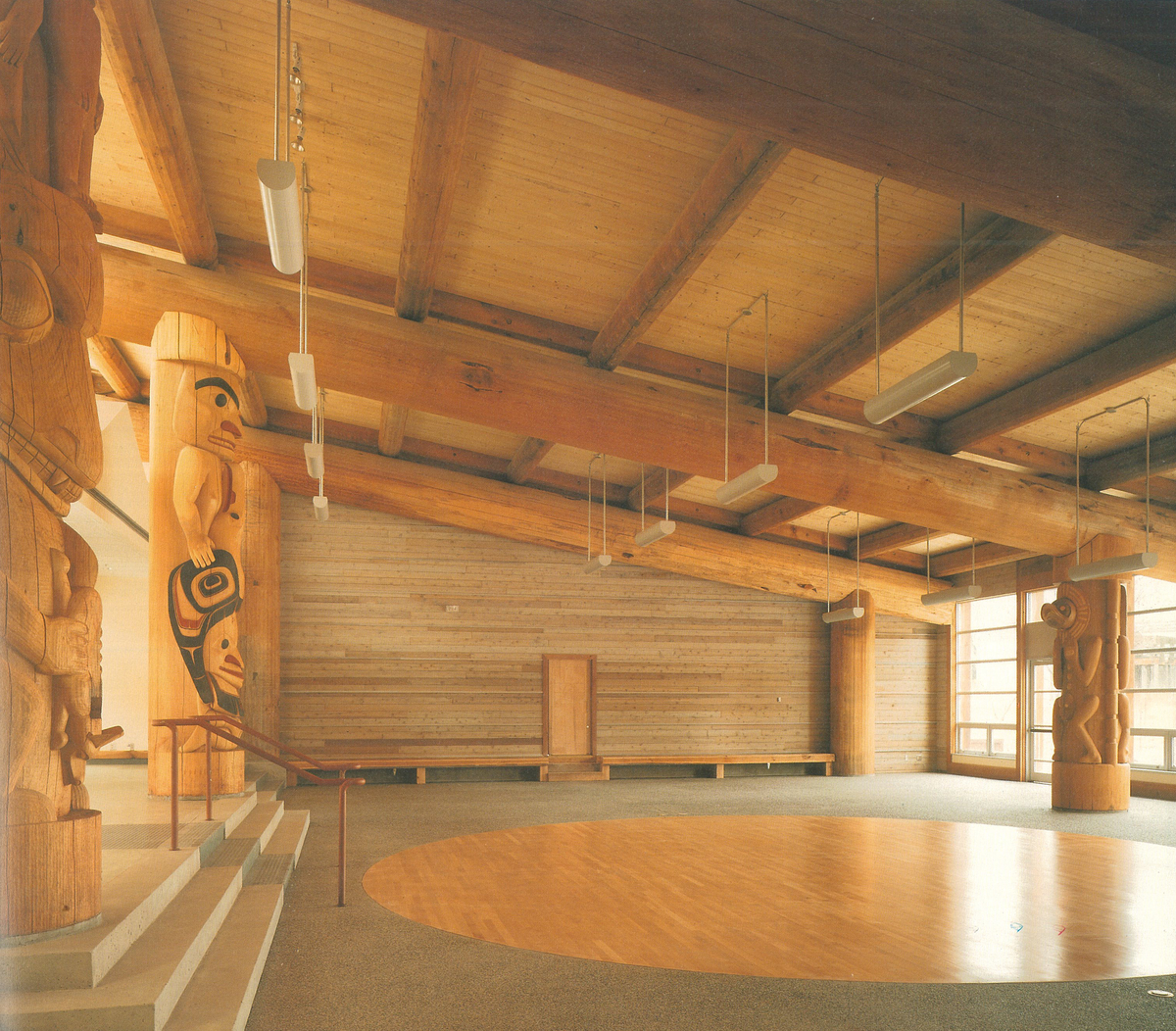 Indoor daytime image of First Nations Longhouse central room at The University of British Columbia showing massive pole beams and columns near the four striking cedar houseposts; hand-carved and a metre in diameter