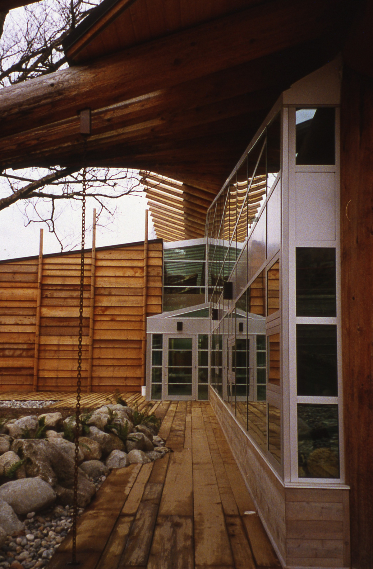 Outdoor daytime close up image of First Nations Longhouse at The University of British Columbia showing glass and wood exterior topped with mass timber solid sawn heavy timber roof structure designed to resemble the wing of a bird in flight