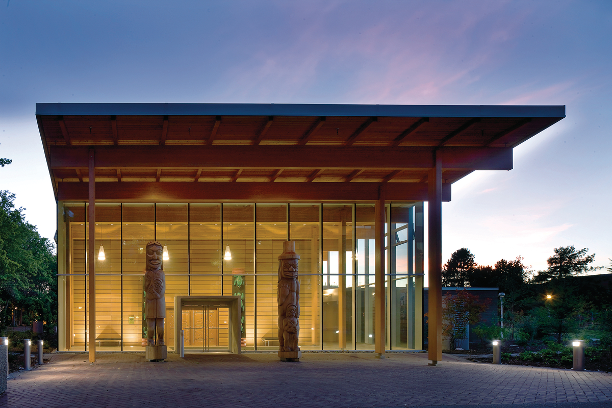 Exterior evening view of low rise First Peoples House showing post and beam columns supporting Douglas-fir glue-laminated timber (glulam) beams and sloping wood roof