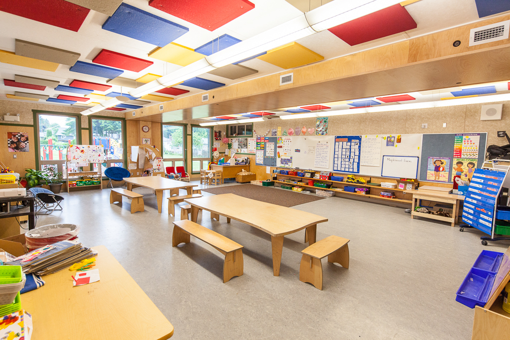 Internal daytime view of low rise Full Day Kindergarten Classrooms showing abundant use of wood, including desks, chairs, HVAC duct paneling, wall paneling, and additional millwork