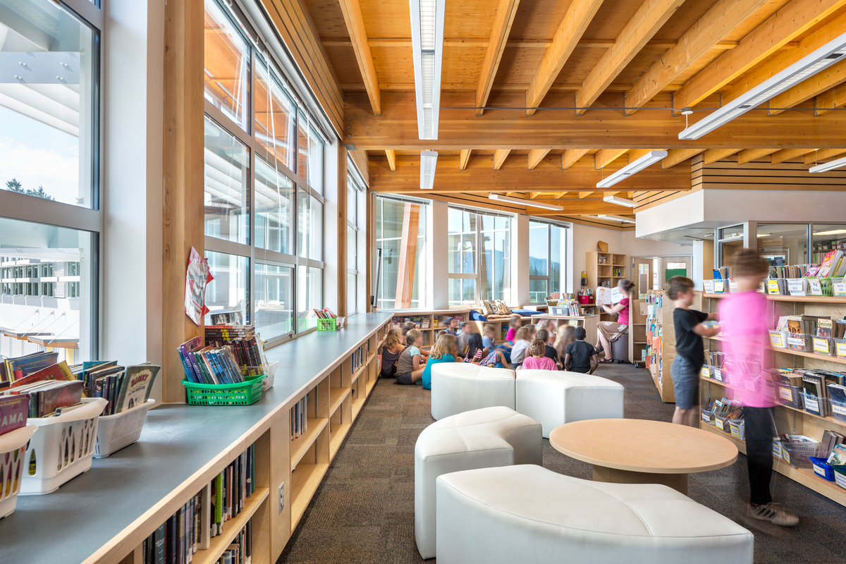 Interior daytime view of children and librarian inside glass fronted Gibsons Elementary School library area complete with structural Glue-laminated timber (glulam) beams and columns structural materials