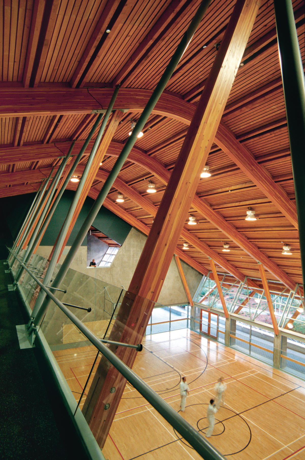 Interior daytime view of low rise Gleneagles Community Centre showing four story main gymnasium, including a huge shed-like roof composed of prefabricated wood panels, supported by Douglas-fir glue-laminated timber beams