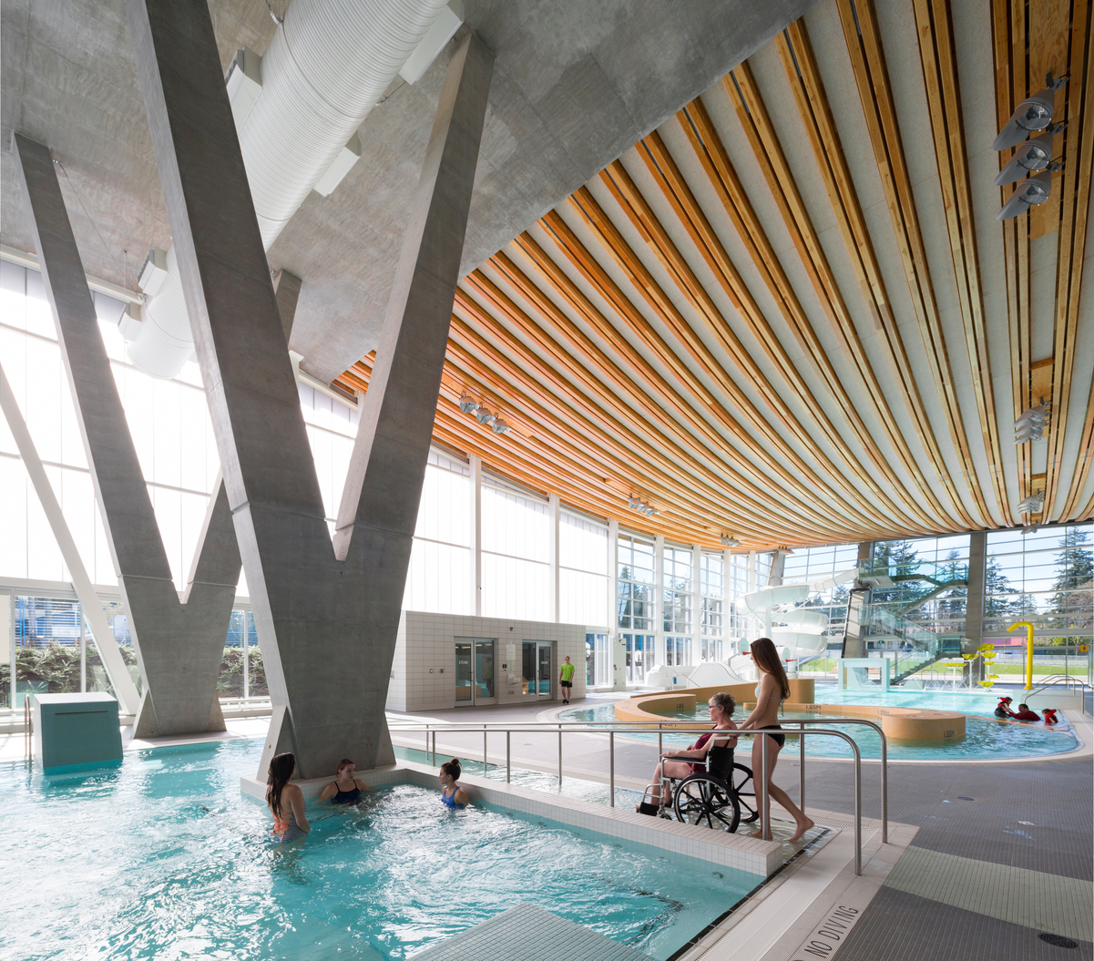 Interior daytime view of Grandview Heights Aquatic Centre family activity area showing families below with glulam-cable prefab roof assembly above