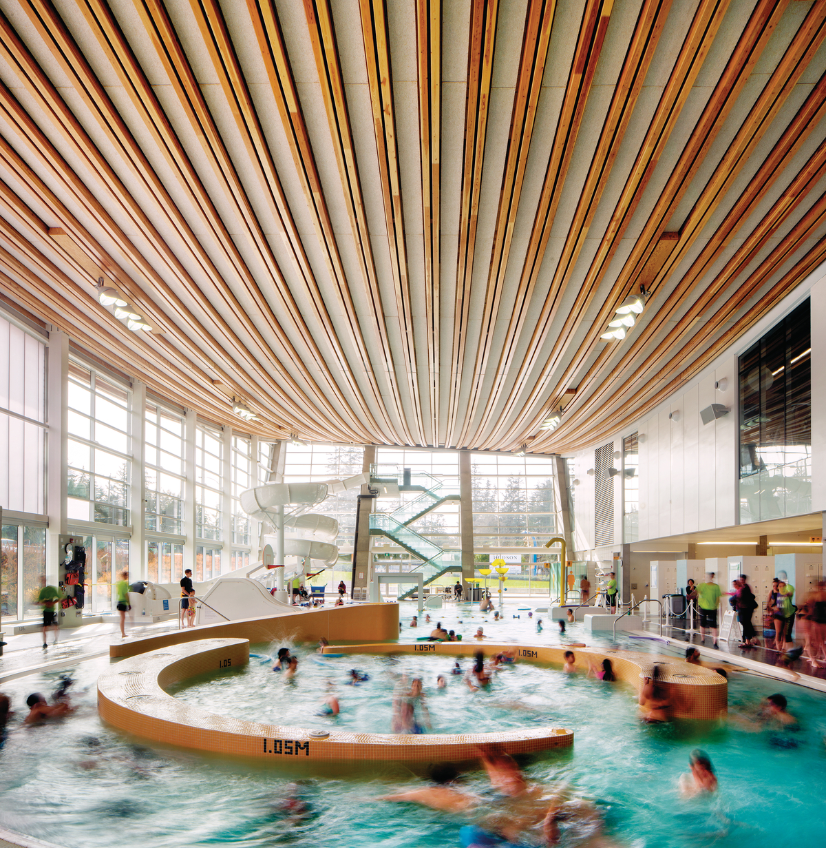 Interior daytime view of Grandview Heights Aquatic Centre family activity area showing families playing in water below with glulam-cable prefab roof assembly above