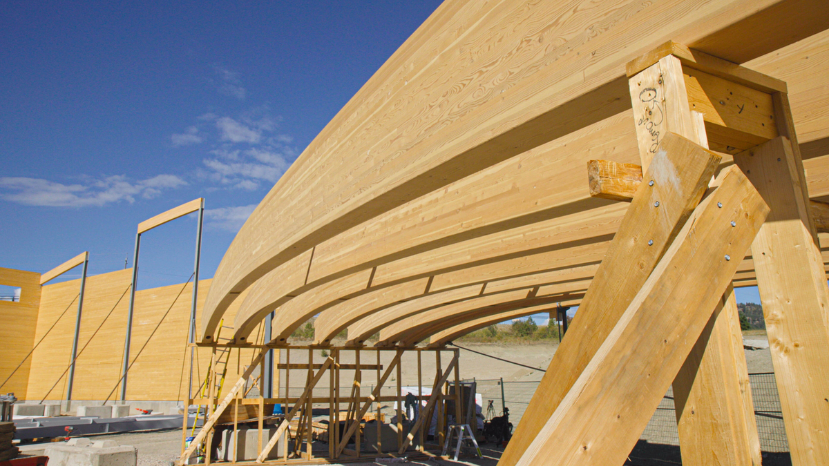Arched CLT beams extend from the right side through to the center of the frame, at a construction site.