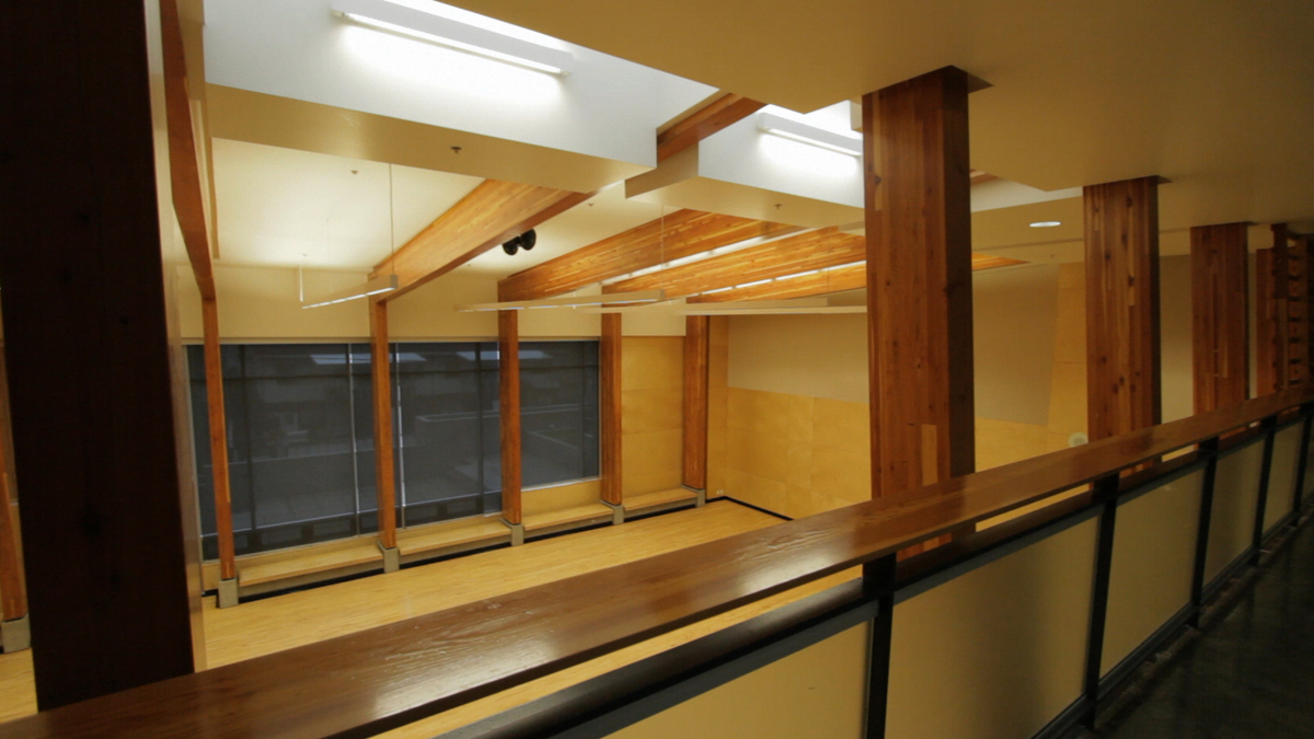Interior second floor view of King David High School balcony walkway, looking down on the multi-purpose sanctuary, with wood floors and exposed glue-laminated timber (glulam) beams and columns