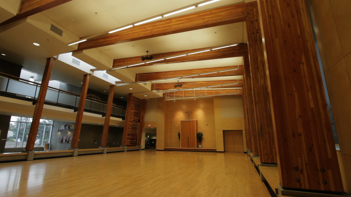 Interior daytime upward view of King David High School multi-purpose sanctuary, with wood floors and exposed glue-laminated timber (glulam) beams and columns