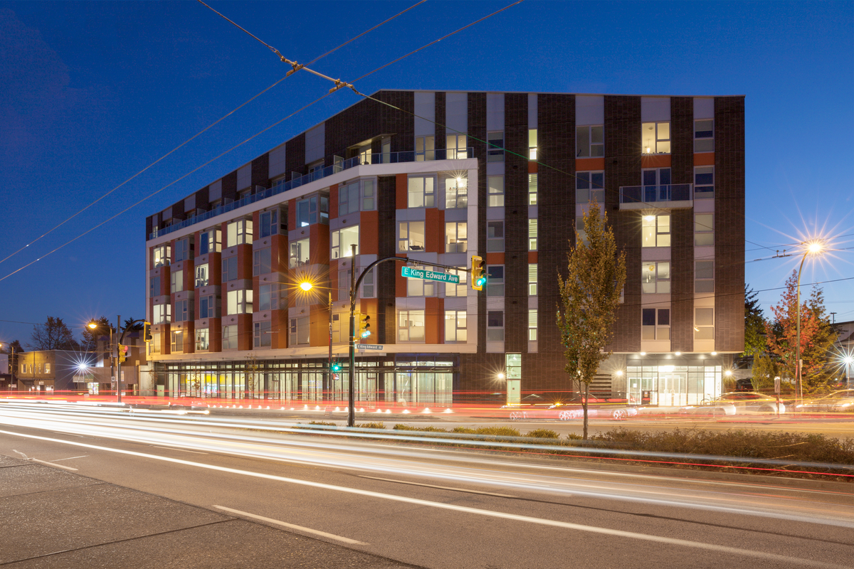 Exterior nighttime view of the six-storey King Edward Villa, a mixed use budling constructed using prefabricated wood construction along with hybrid / wood and light frame systems