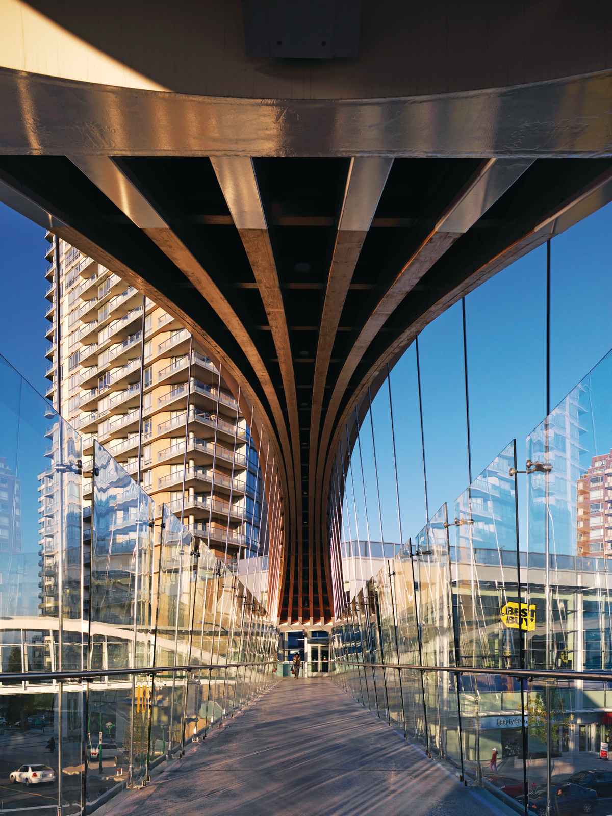 Exterior daytime view from deck of Kingsway Pedestrian Bridge, showing double-curved glue-laminated timber (glulam) arch above, with walkway suspended by steel cables below
