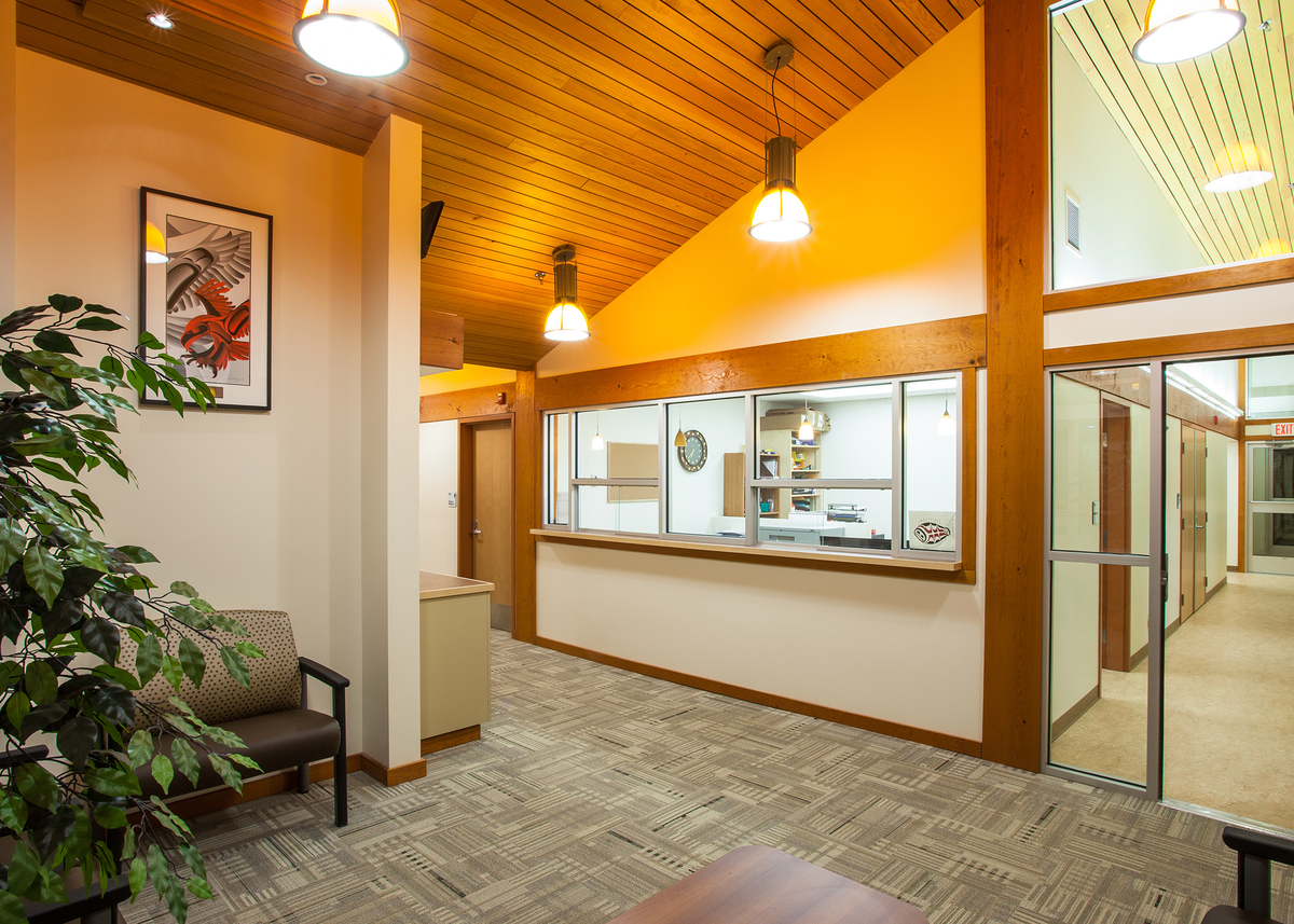 Interior daytime view of low rise Kitsumkalum Health Centre, showing extensive use of wood trim and accents, including wooden ceiling and paneling