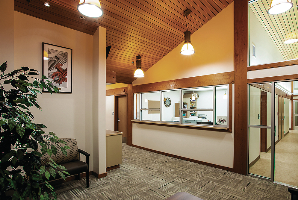 Interior daytime view of low rise Kitsumkalum Health Centre, showing extensive use of wood trim and accents, including wooden ceiling and cladding