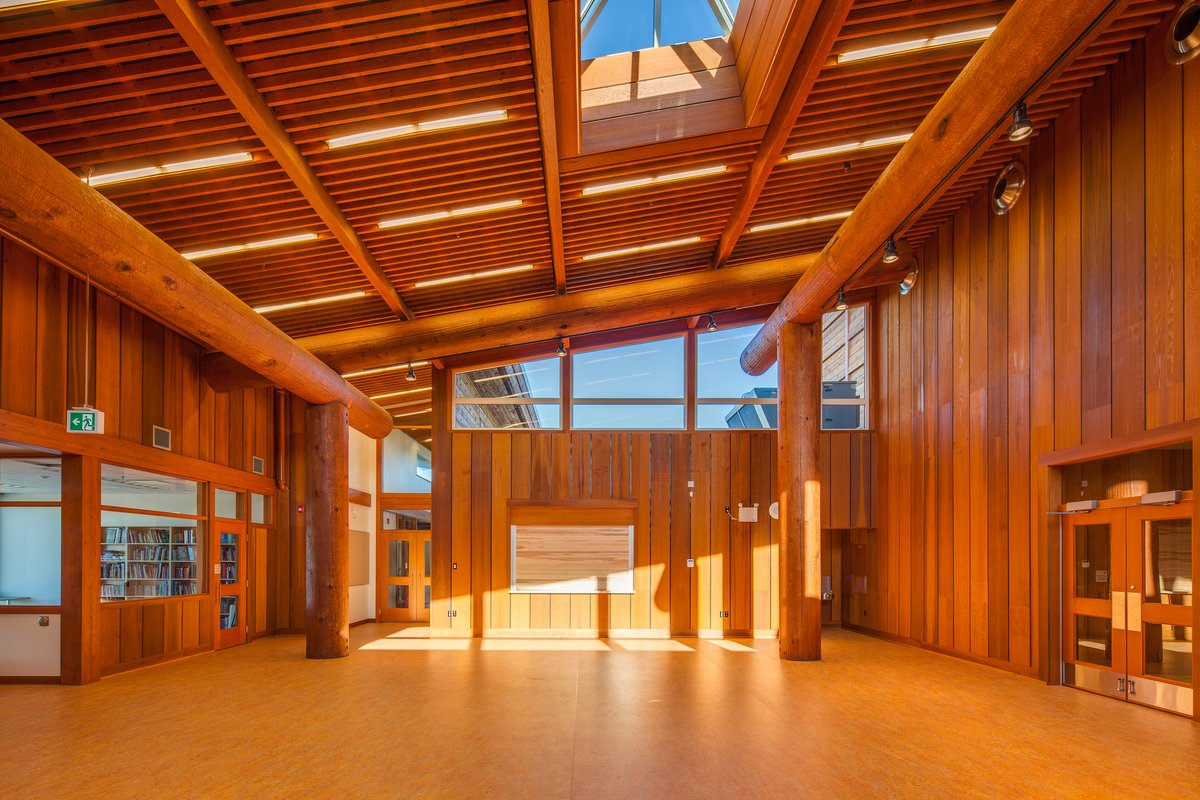Sunny daytime interior view of low rise Kwakiutl Wagalus School bright sunny main entrance and 2 story atrium showing extensive use wood, including western red cedar in posts, beams, and cladding, Douglas-fir for doors and windows, birch wood veneer finishes, and a wood flooring