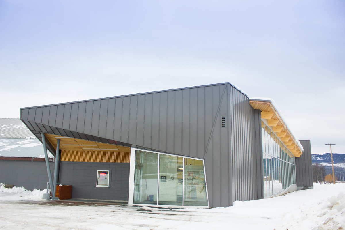 Exterior snowy daytime view of Lakeside Multiplex showing exterior metal siding with an exposed roof structure consists of solid plank decking and glue-laminated timber (glulam) beams that extend beyond the outer walls, creating a wood soffit