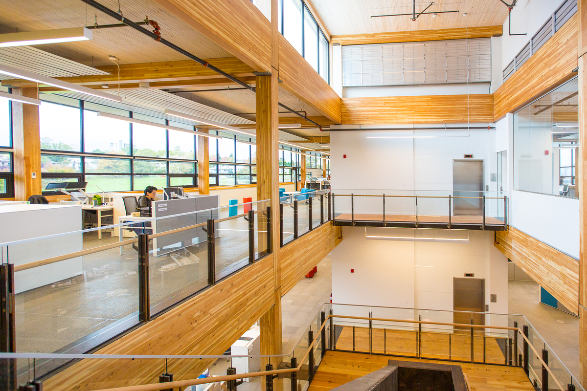 Interior view of completed MEC Headquarters building from top of multi storey half turn stairwell, showing brightly lit interior with communal and isolated working area, with mass timber construction, including: glue-laminated timber (Glulam), nail-laminated timber (NLT), and abundant millwork