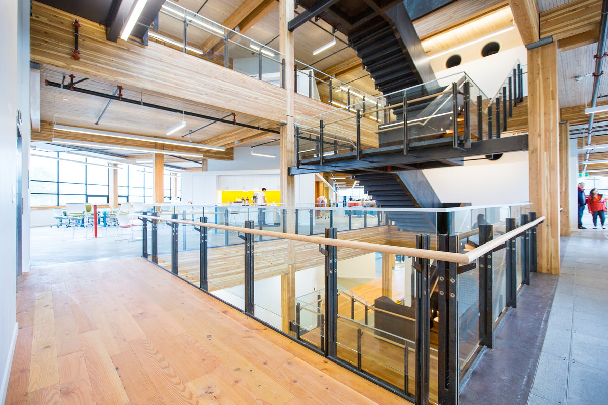 Interior view of completed MEC Headquarters building showing multi storey half turn stairwell, communal working area, and mass timber construction, including: glue-laminated timber (Glulam), nail-laminated timber (NLT), and abundant millwork