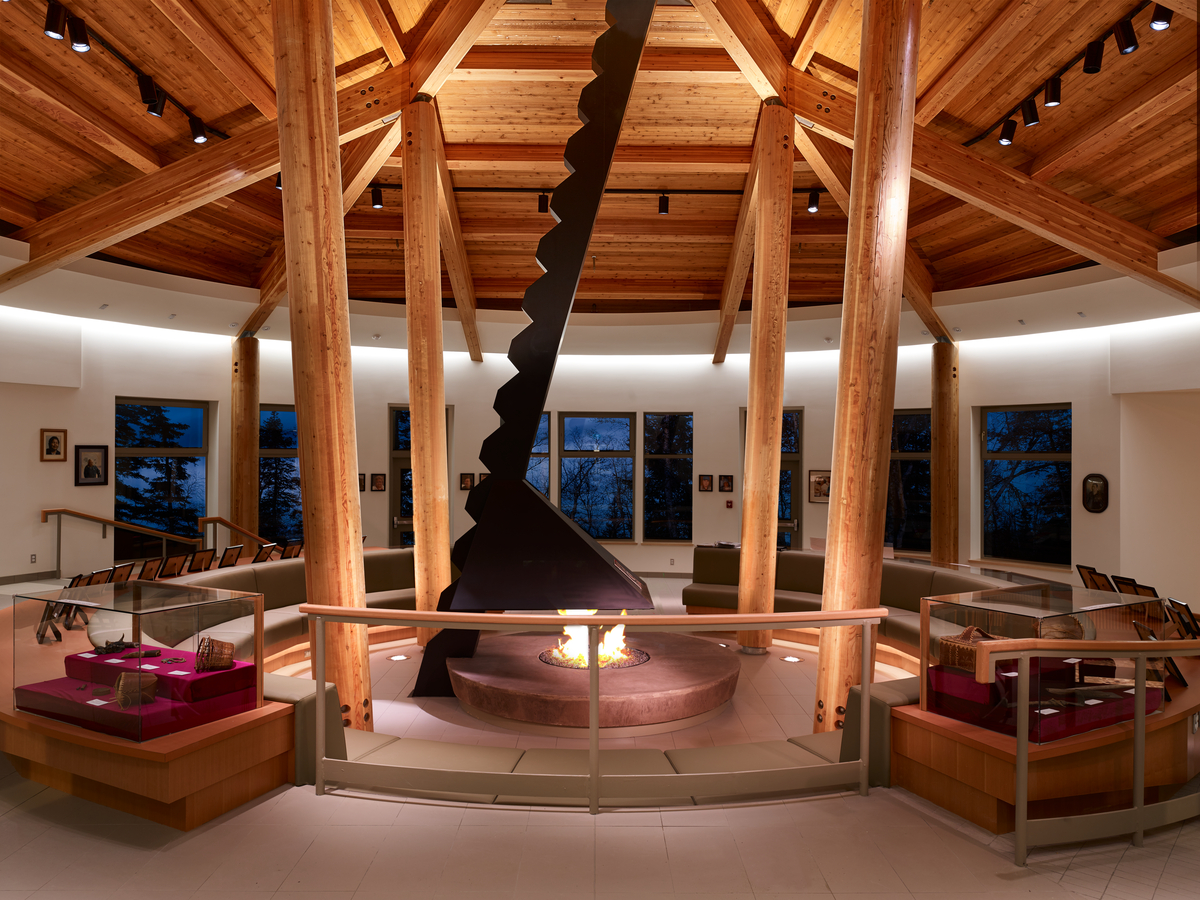 Inside evening view of Nadleh Whutenne Yah Administration and Cultural Building showing circular lobby, with an exposed vaulted glue-laminated timber (glulam) beam roof finished in western red cedar tongue-in-groove planks and fire pit in middle
